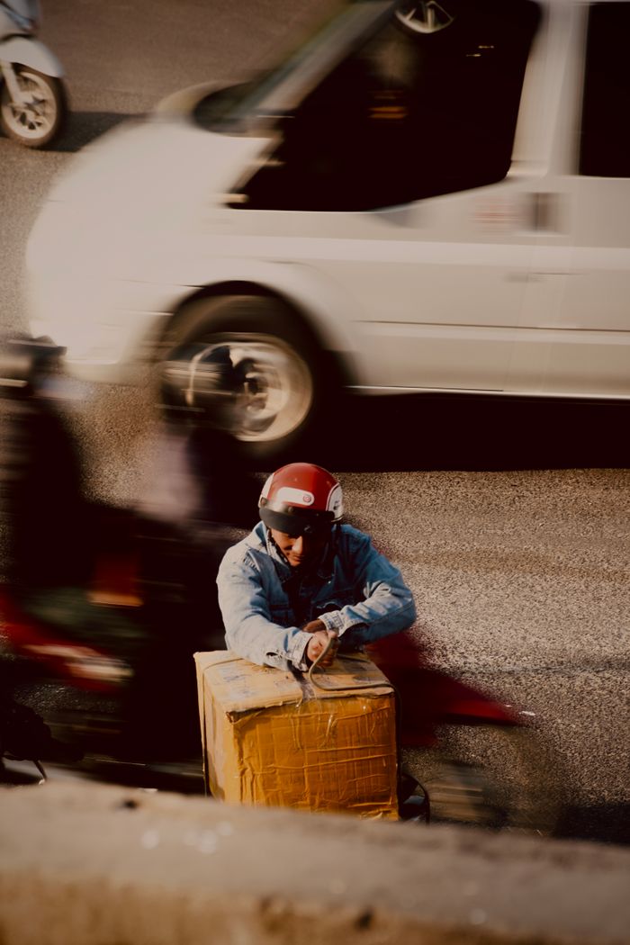 Motorbike courier with package on Hanoi street amidst fast-moving traffic and motorbikes.