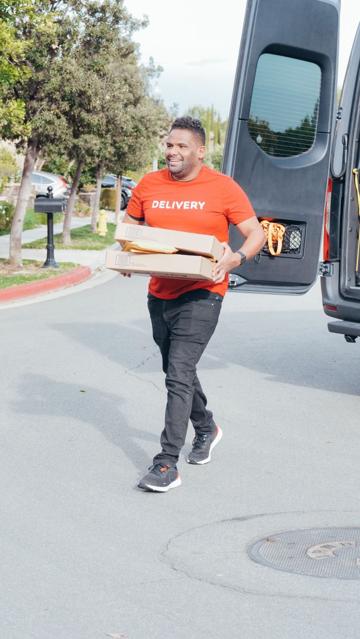 services-04 Delivery man in red shirt carrying package from van on a sunny street.